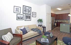 Newton apartment for rent - Living room with open layout, hardwood floors and view of kitchen; model pictured with gallery wall, coffee table and couches