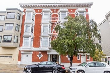 San Francisco apartment for rent - A black car is parked in front of a red brick building with a tree in front of it.