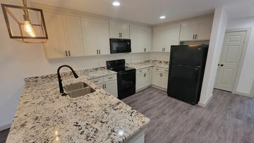 Denton triplex for rent - a kitchen with white cabinets and black appliances and granite counter tops