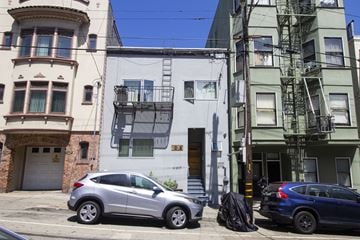 San Francisco apartment for rent - A white car is parked in front of a white building with a fire escape.