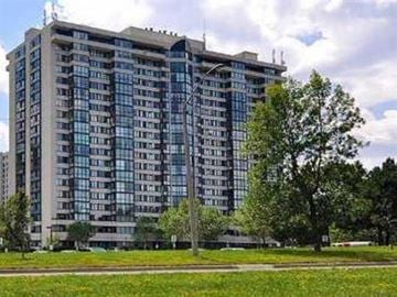 Toronto apartment for rent - A large, modern building with many windows is surrounded by trees and grass.