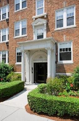 Cambridge apartment for rent - the front entrance of a brick building with bushes and a sidewalk