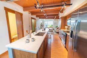 Seattle apartment for rent - Modern kitchen with large island, stainless steel appliances, wood beam ceilings, and open view into the living room.