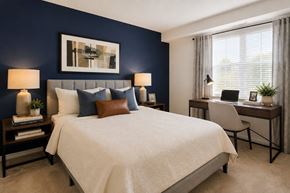 Baltimore apartment for rent - A bedroom with a large bed, a desk with a chair, and a painting on the wall.