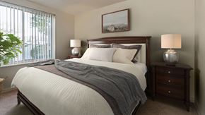 Hyattsville apartment for rent - A bedroom with a large bed, a nightstand, and a window with blinds.