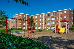 Hyattsville apartment for rent - A playground with a red swing set in front of a red brick apartment building.