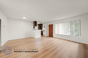 Long Beach apartment for rent - A spacious room with wooden flooring and a logo for Beach Front Property Management in the corner.