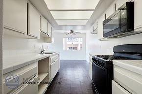 Long Beach apartment for rent - A clean, white kitchen with black appliances and a logo for Beachfront Property Management in the corner.