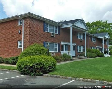 Denville apartment for rent - A red brick building with white trim and a green bush in front.