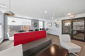 Omaha apartment for rent - A modern office space with a red and grey couch, a wooden table, and a glass door leading to another room.