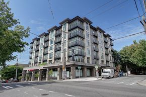 Seattle apartment for rent - A large apartment building with balconies and a red awning is situated on a street corner.
