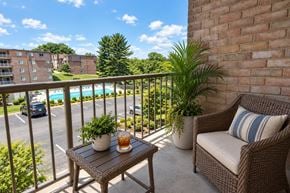 Glen Burnie apartment for rent - A balcony with a table, chairs, and a view of a pool and buildings.