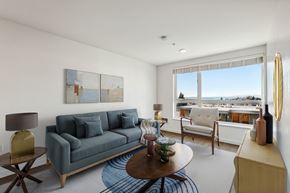 Seattle apartment for rent - Spacious living room at 4400 Alaska with blue sofa, armchair, and a large window offering an outd...