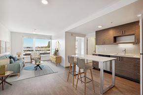 Seattle apartment for rent - Open-concept living room with a blue sofa, large window, and integrated kitchen with an island an...