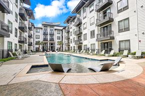 Dallas apartment for rent - A large swimming pool surrounded by lounge chairs and buildings.