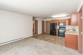 West Fargo apartment for rent - an empty living room with a kitchen with a black refrigerator