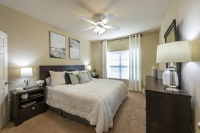 San Antonio apartment for rent - A bedroom with a large bed, a ceiling fan, and a window with curtains.