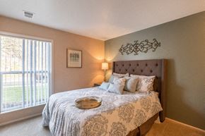 Okemos townhouse for rent - A bedroom with a large bed and a window with blinds.