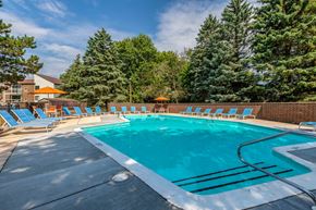 Okemos townhouse for rent - A large outdoor swimming pool surrounded by trees and lounge chairs.