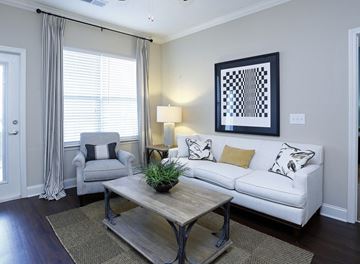 Sanford apartment for rent - A living room with a white couch, a grey armchair, a wooden coffee table, and a painting on the wall.