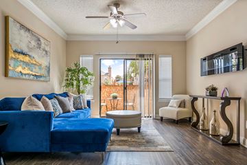 Houston apartment for rent - A blue couch sits in a living room with a painting on the wall and a ceiling fan.