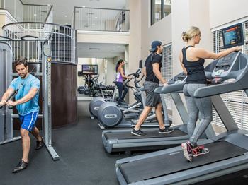 Four people working out in 24-hour fitness center with treadmills and elliptical machines