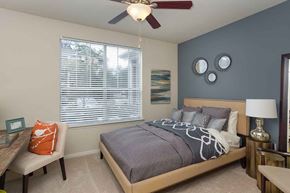The Woodlands apartment for rent - Apartments for Rent in The Woodlands TX - Whispering Pines Ranch - Furnished Bedroom With Comfortable Bed, a Ceiling Fan, and a Desk With a Chair on Top of Carpet Flooring