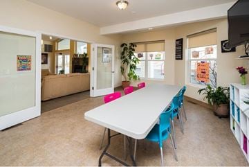 Anchorage townhouse for rent - A white dining table with blue chairs is in the center of a room with a glass door leading to a living room.