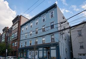 Jersey City apartment for rent - A blue building with a white roof is in the foreground with a clear blue sky above.