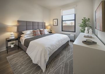 Jersey City apartment for rent - A bedroom with a large bed and a window overlooking a cityscape.