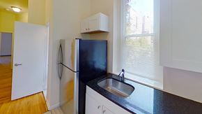 Jersey City apartment for rent - A black fridge in a kitchen with white cabinets and a wooden floor.
