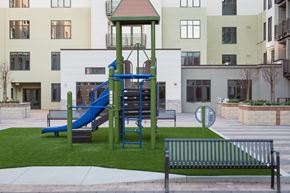 Cupertino apartment for rent - Pet Friendly Apartments in Cupertino CA - Nineteen800 - Playground with Slide, Climbing Equipment, Artificial Grass, Benches, Planters, and View of Apartment Building in the Background at Nineteen800 