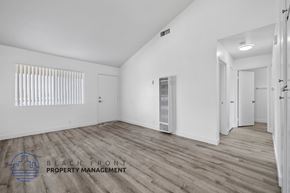 Long Beach apartment for rent - A spacious room with wooden flooring and white walls, with a logo for Beach Front Property Management in the bottom left corner.