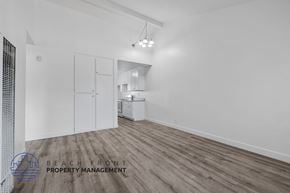 Long Beach apartment for rent - A spacious room with wooden flooring and white walls, with a kitchen area visible in the background.