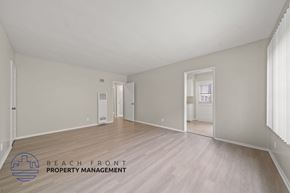 Downey apartment for rent - A spacious room with wooden flooring and white walls, with a door on the left and a window on the right.