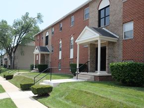 Baltimore apartment for rent - A red brick building with a white porch and a black railing.