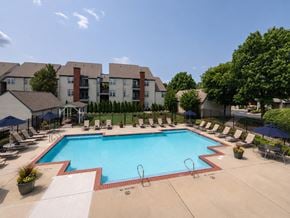 Cherry Hill apartment for rent - A large swimming pool surrounded by lounge chairs and umbrellas in front of apartment buildings.