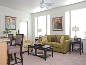 Corpus Christi apartment for rent - A living room with a green couch, a chair, a table, and a ceiling fan.