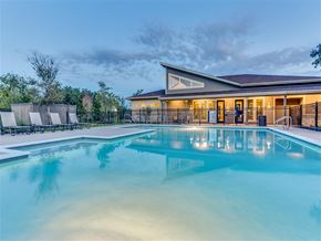 San Antonio apartment for rent - A large swimming pool in front of a building with a fence and trees in the background.