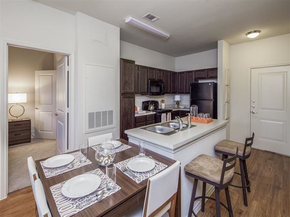 Fort Worth apartment for rent - Open-concept kitchen and dining area featuring a breakfast bar with seating, dark cabinetry, modern appliances, and a dedicated dining space with direct access to the adjacent bedroom.