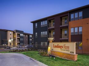 Fort Worth apartment for rent - Community entrance sign for Landings at Marine Creek Apartment Homes, with apartment buildings, landscaped grounds, and gated community access visible in the background.