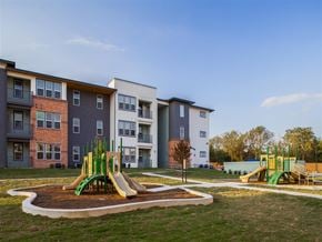 San Marcos apartment for rent - Community playground area featuring multiple play structures, landscaped walking paths, open green space, and surrounding apartment buildings.