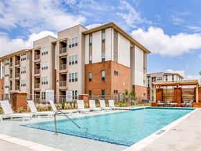 Dallas apartment for rent - A swimming pool is surrounded by sun loungers in front of apartment buildings.