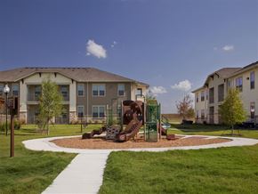 Karnes City apartment for rent - A playground in front of apartment buildings on a sunny day.