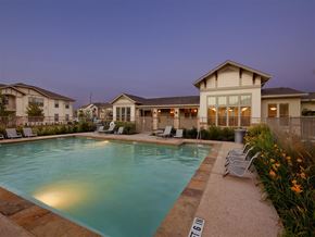 Karnes City apartment for rent - A pool surrounded by chairs and a building in the background.