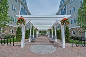 Tewksbury apartment for rent - A walkway with a white pergola and hanging flower baskets leads to a building.