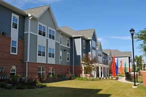 Cleveland apartment for rent - A building with grey and white siding and a red brick base with a black lamp post in front.