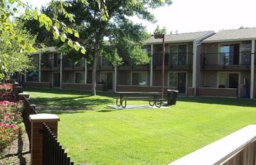 Boise apartment for rent - a bench in the middle of a lawn in front of an apartment building