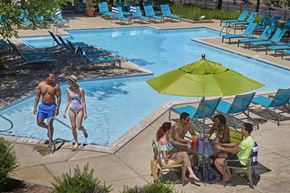 Auburn Hills apartment for rent - A group of people are sitting around a table under a green umbrella by a pool.