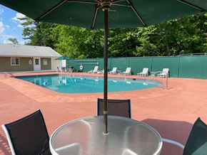 Milford apartment for rent - A pool with chairs and umbrellas is surrounded by a green fence.